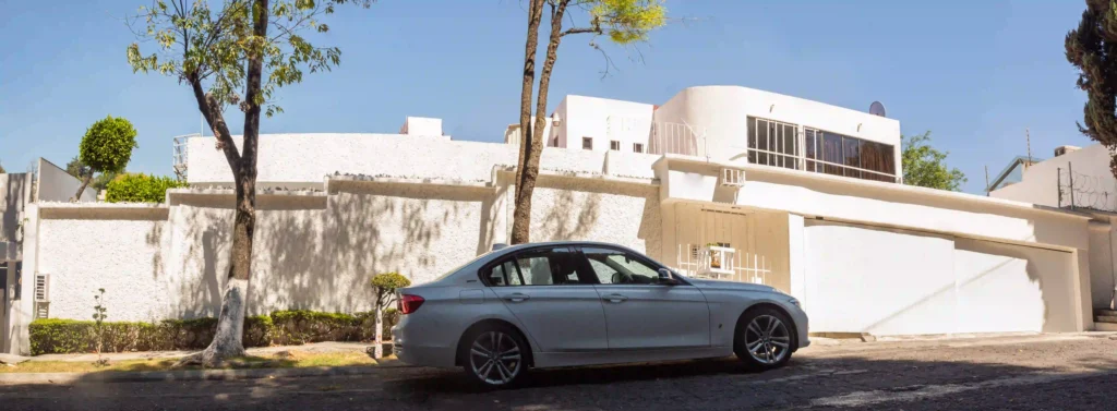 Fachada principal de casa moderna en Bosques de las Lomas con portón blanco, cochera techada y jardín frontal, Ciudad de México