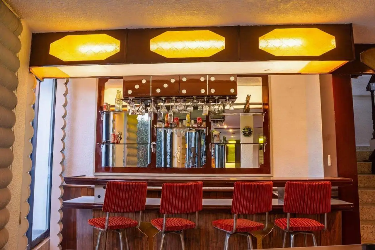 Bar interior retro con barra de madera, taburetes rojos y luces cálidas en casa de lujo en Bosques de las Lomas