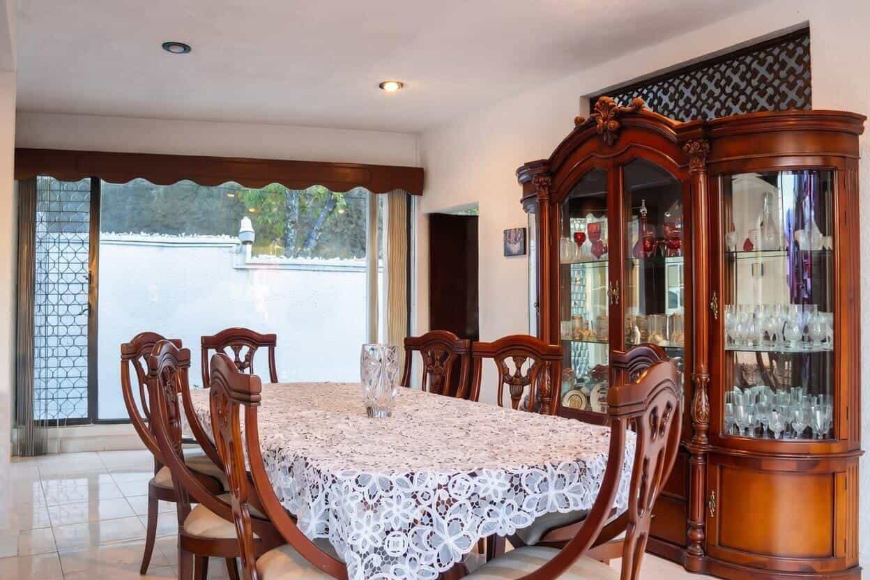 Comedor formal amplio con mesa rectangular grande, sillas talladas y vitrina de madera con cristalería en casa Bosques de las Lomas