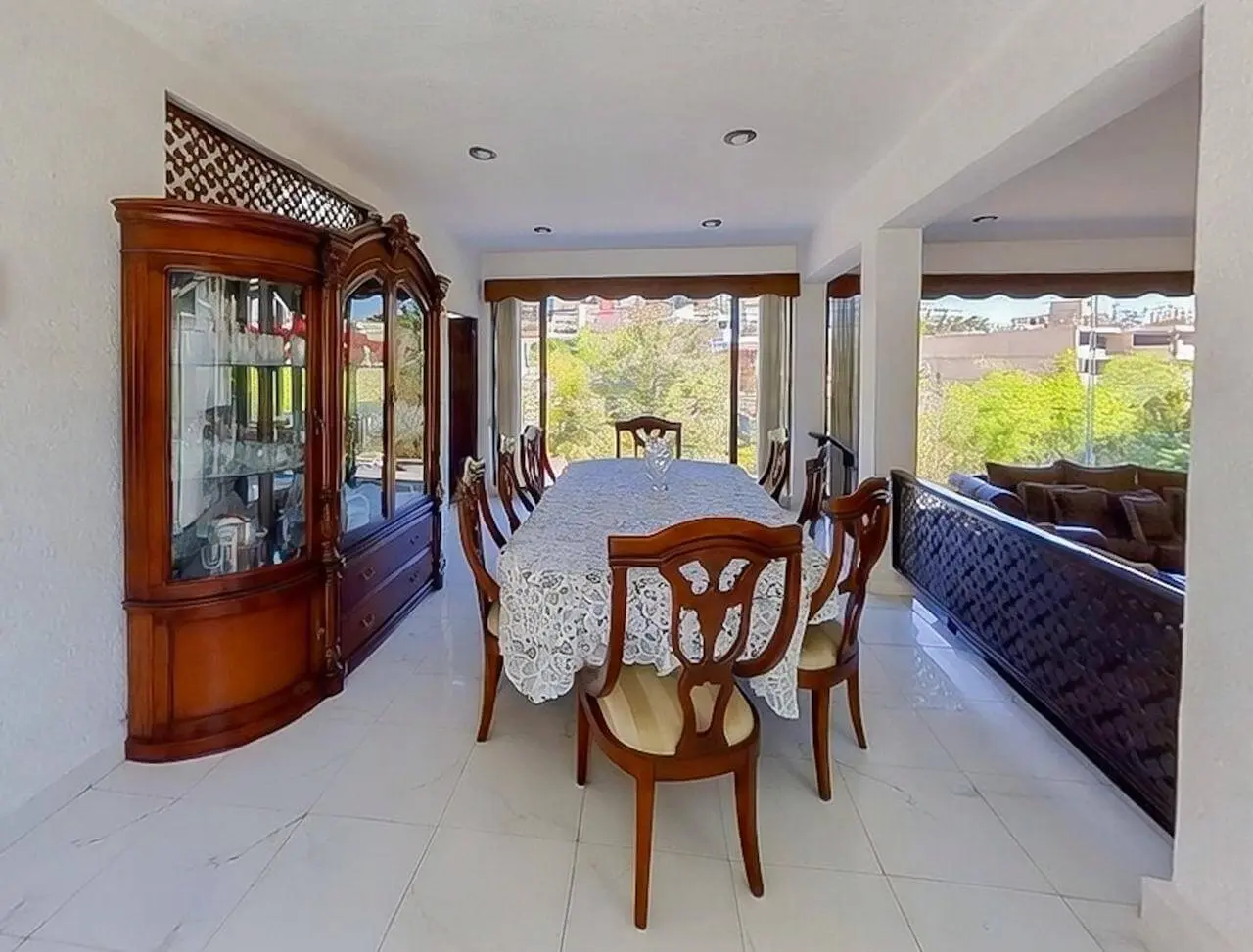 Comedor formal amplio y alargado con mesa rectangular extensa, vitrina grande y ventanales panorámicos al jardín en casa Bosques de las Lomas