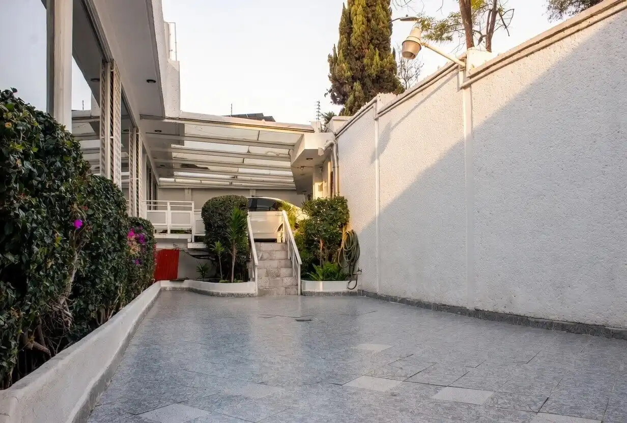 Acceso vehicular y estacionamiento cubierto en casa de lujo en Bosques de las Lomas, con rampa de entrada y vegetación exuberante