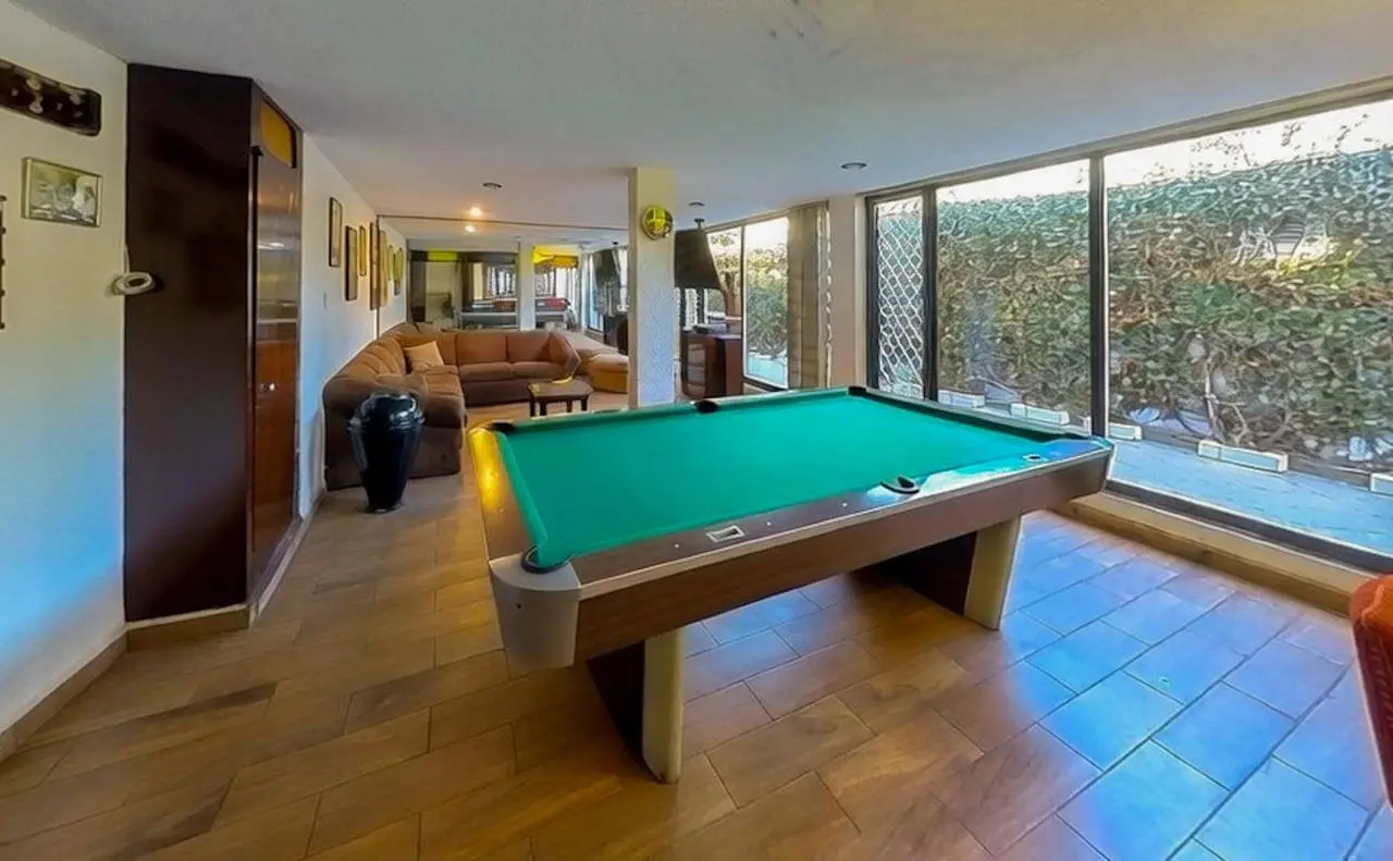 Amplia sala de entretenimiento con mesa de billar, sofá modular y ventanales al jardín en casa de lujo Bosques de las Lomas