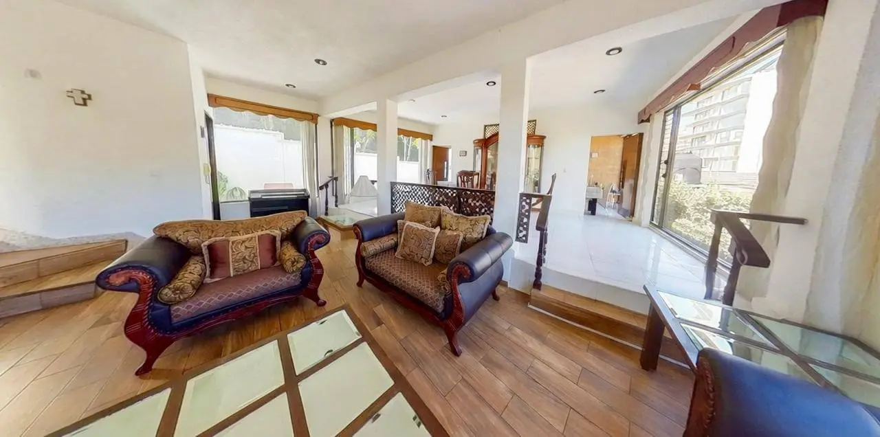 Sala principal amplia y luminosa con sofás clásicos, conexión abierta al comedor y vistas al jardín en casa Bosques de las Lomas