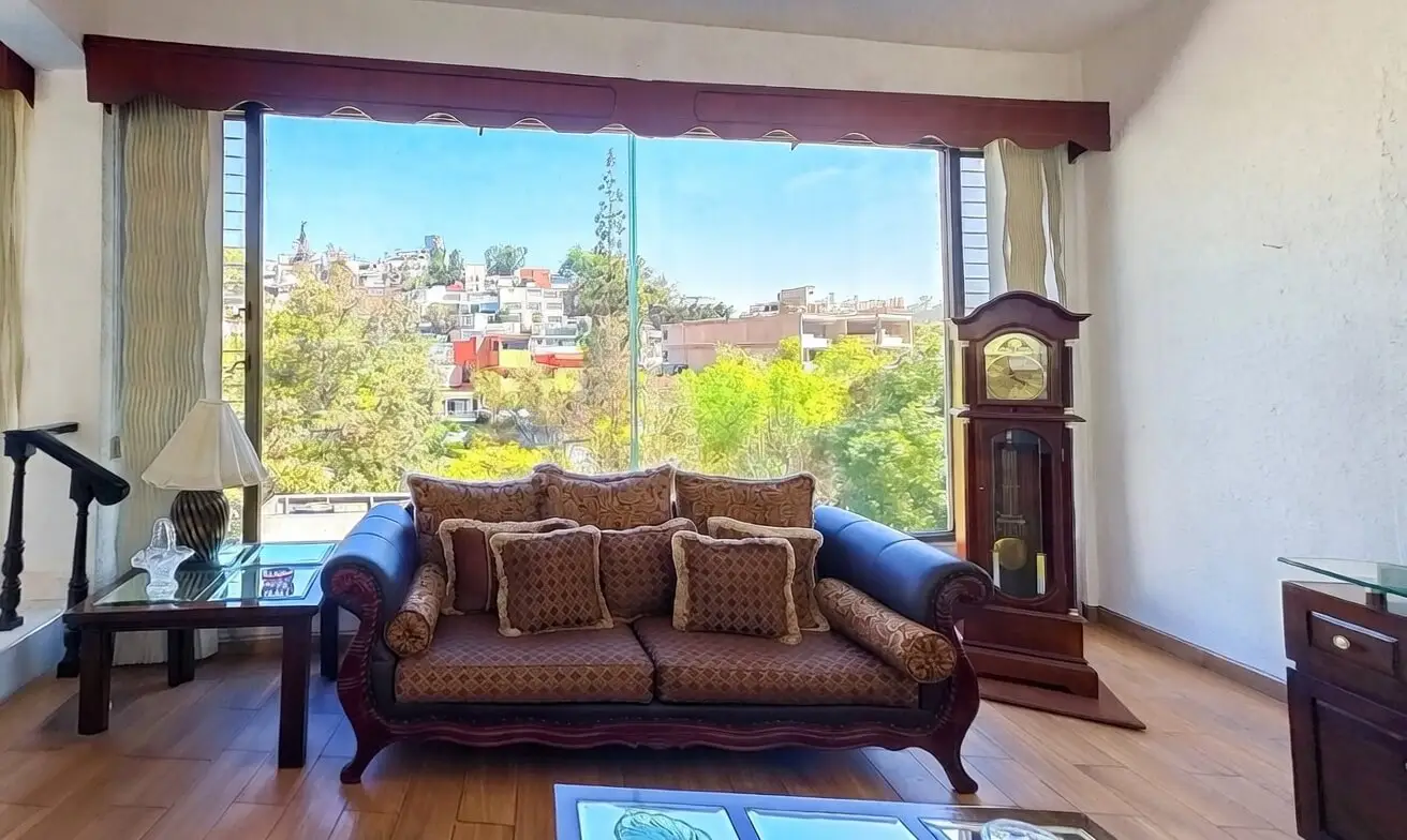 Sala principal formal con sofá clásico, reloj de pie y ventanal panorámico con vistas impresionantes a la ciudad en casa Bosques de las Lomas